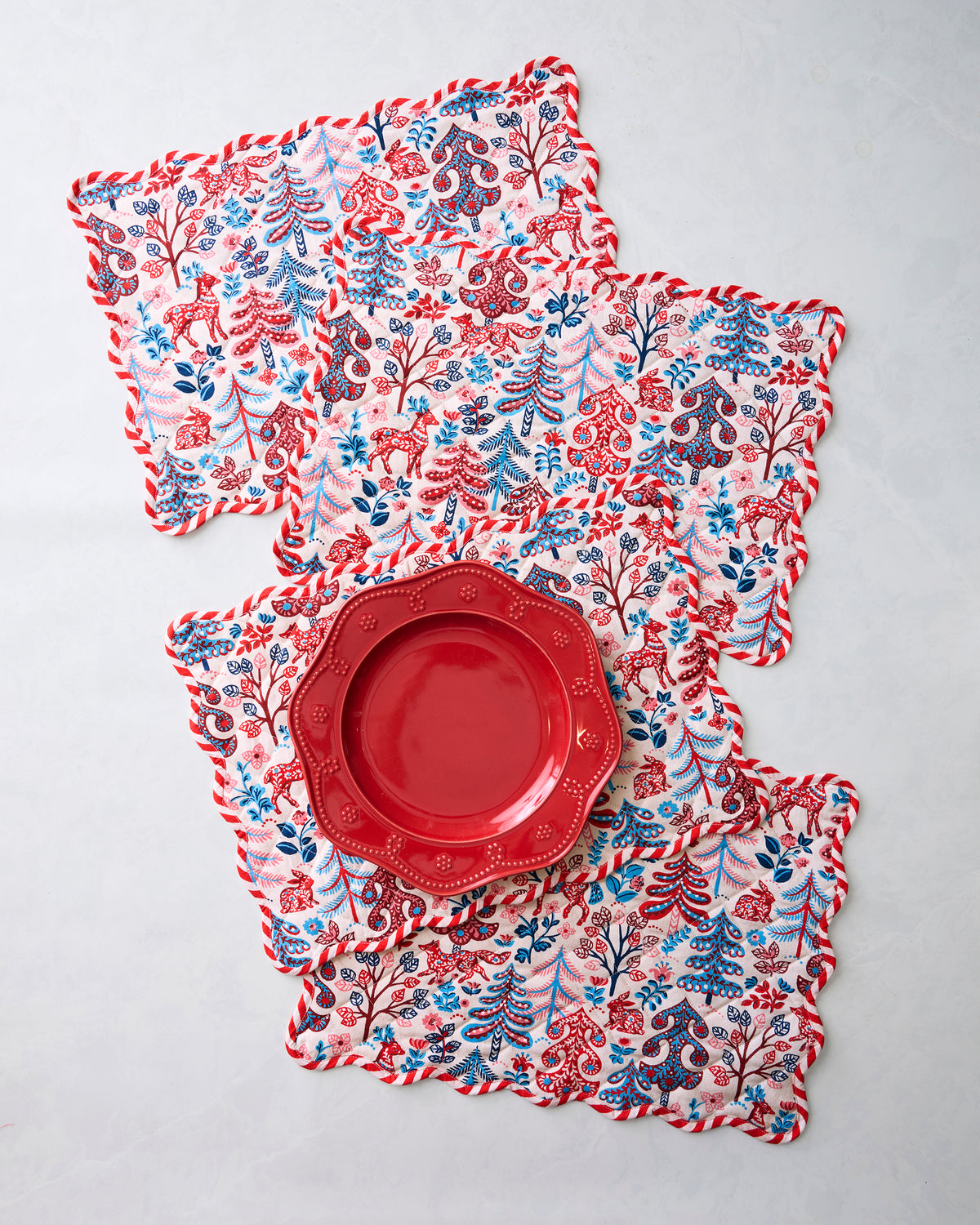 Four Folklore Forest placemats arranged with a red plate placed on top of them.