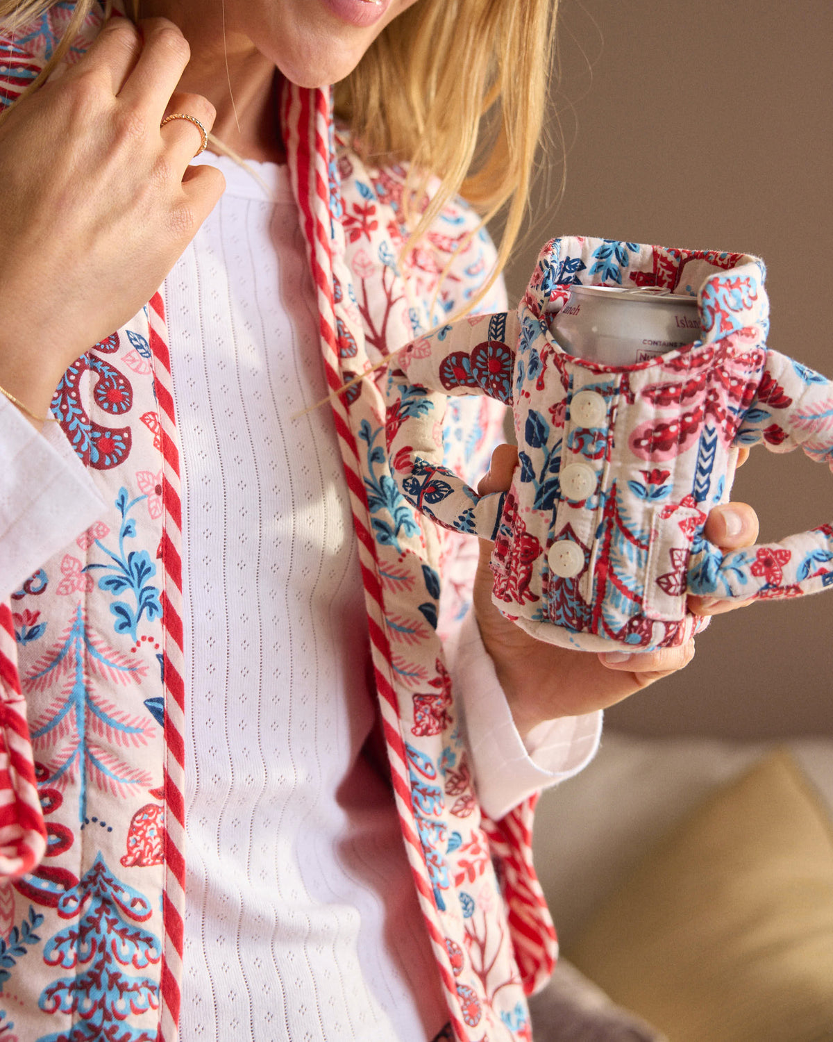 Person holding the cream pajama cozie, showing its button-front design, side handles, and red and blue woodland-pattern print.