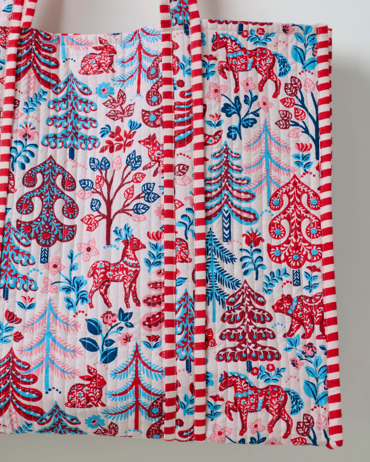 Close-up of the cream tote bag showing its forest and animal print, striped handles, and edge trim.