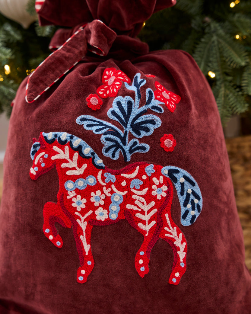 Close-up of the burgundy gift sack’s embroidered red horse and blue floral motif.