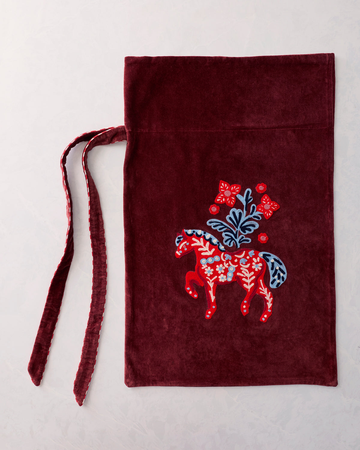 Flat view of a burgundy gift sack with a centered embroidered red horse and floral motif, with two ties extending to the left.