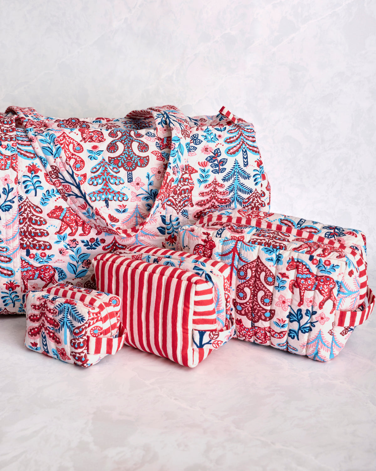 Close-up angled view of a quilted duffle bag and three matching pouches in a red, blue, and cream forest print.