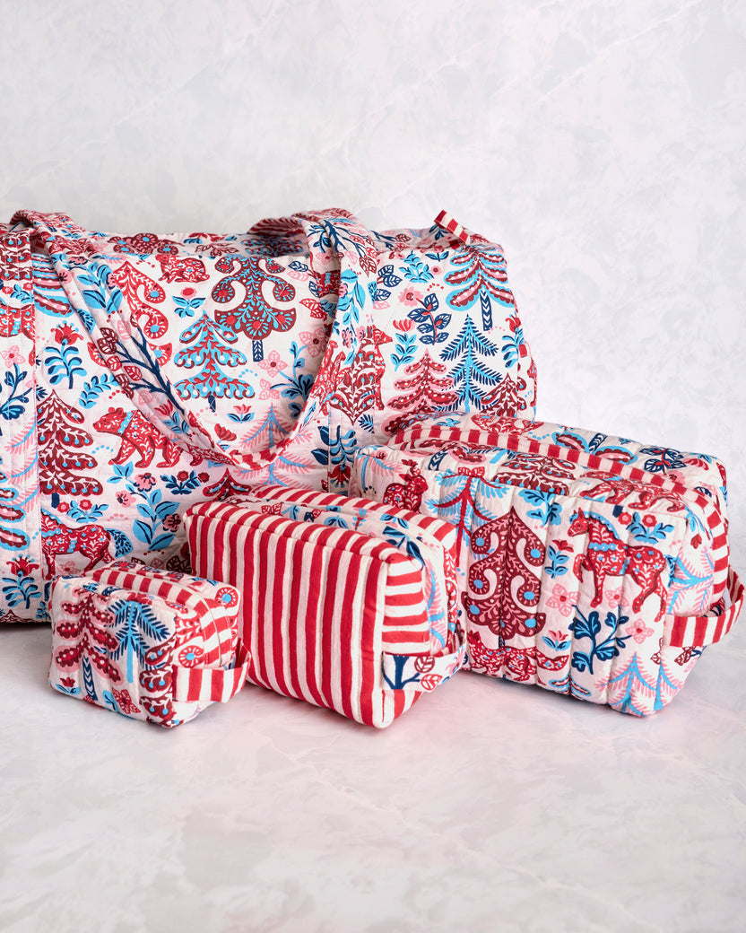 Close-up angled view of a quilted duffle bag and three matching pouches in a red, blue, and cream forest print.