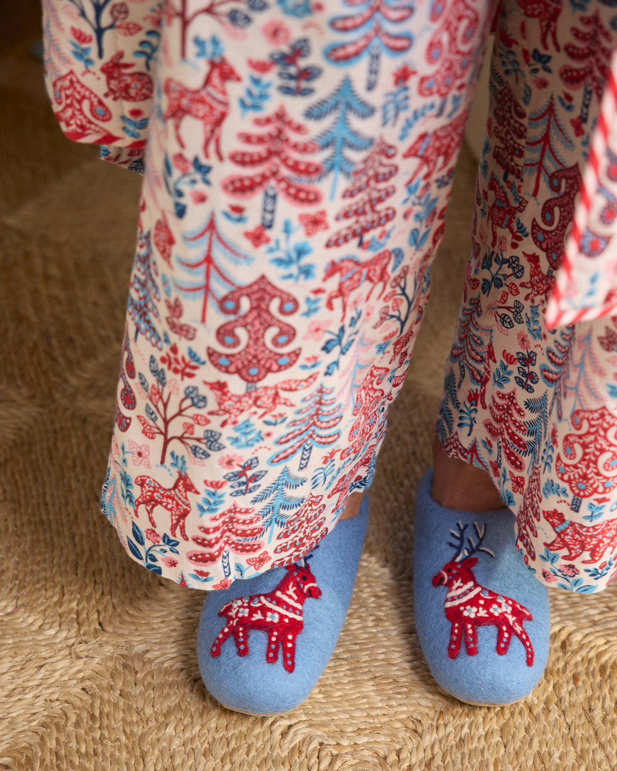 Close-up of light blue slippers with red embroidered deer motifs, worn with printed pajama pants.