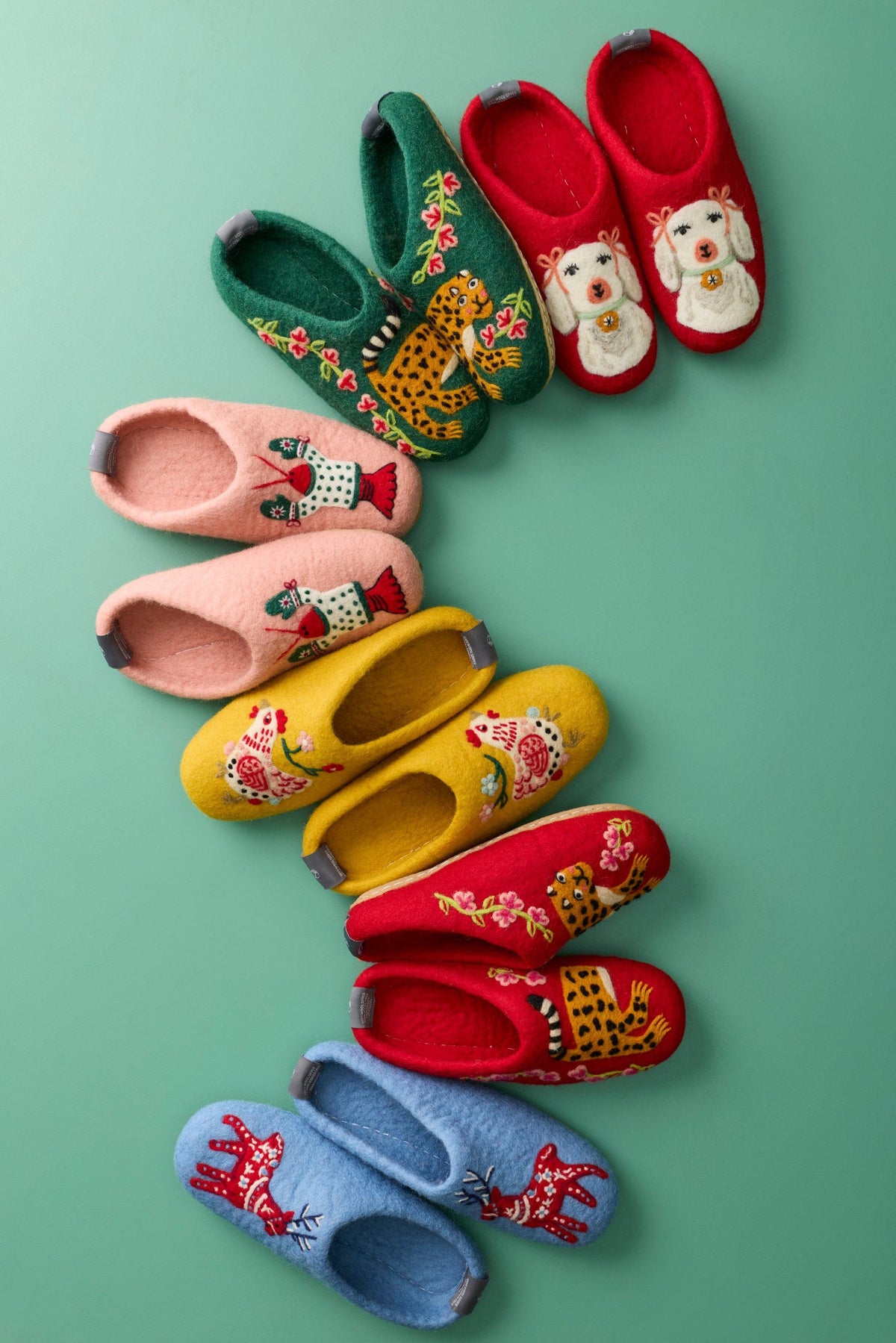 Pairs of colorful embroidered slippers arranged diagonally on a teal background.