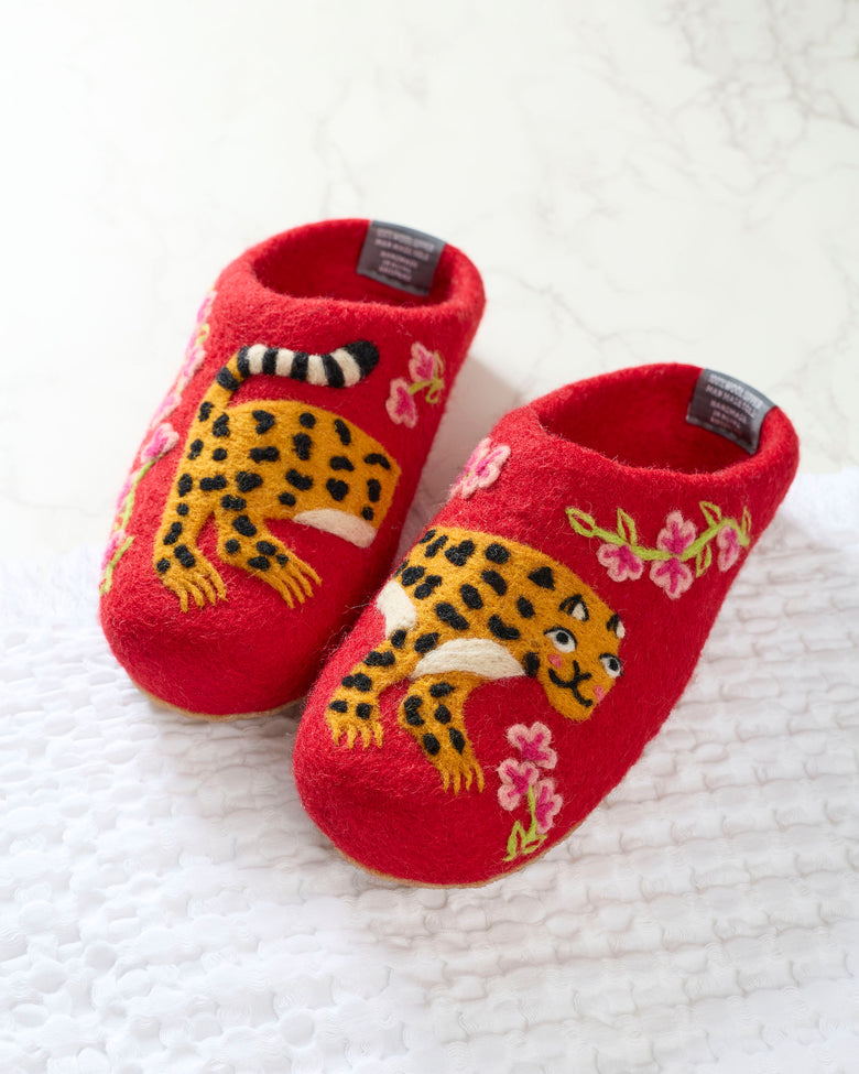 Pair of red slippers with embroidered yellow spotted leopards and pink flowers, photographed on a white textured surface.