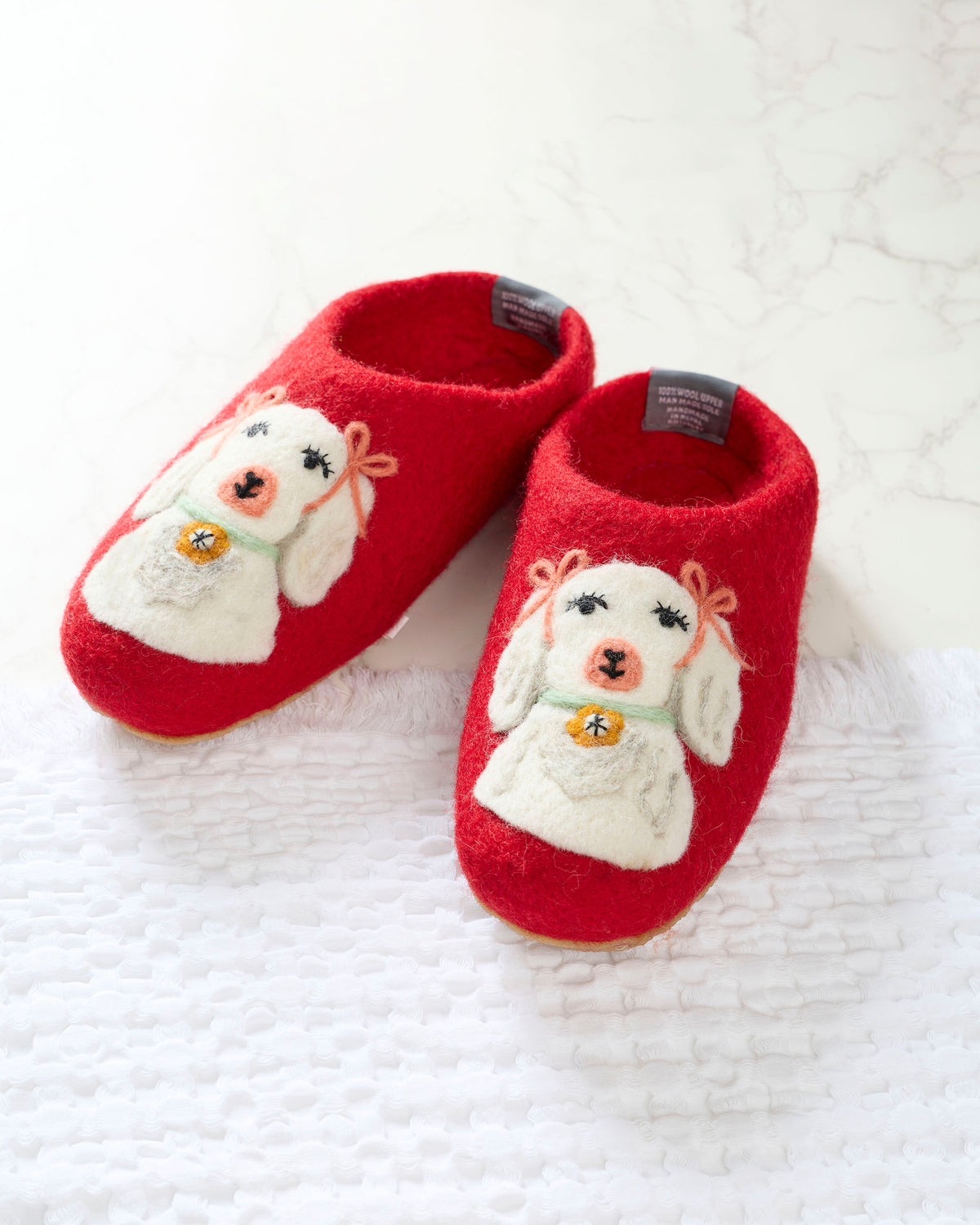 Pair of red slippers with white embroidered dogs wearing green collars and gold bell details.