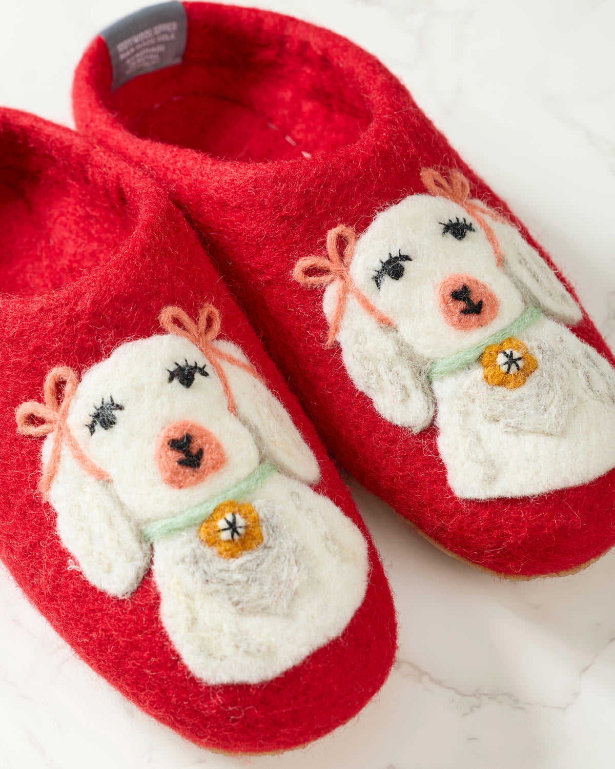 Close-up of red slippers featuring white embroidered dogs with pink bows, green collars, and gold bell details.