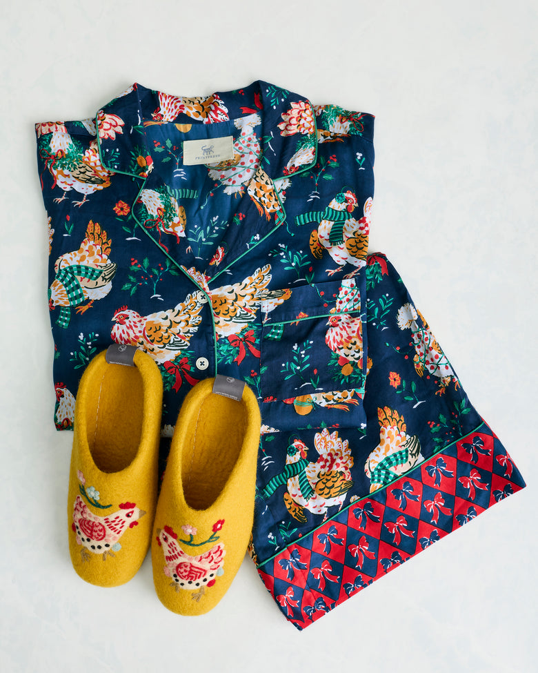 Yellow Holiday Hens slippers displayed with a navy hen-print pajama set.