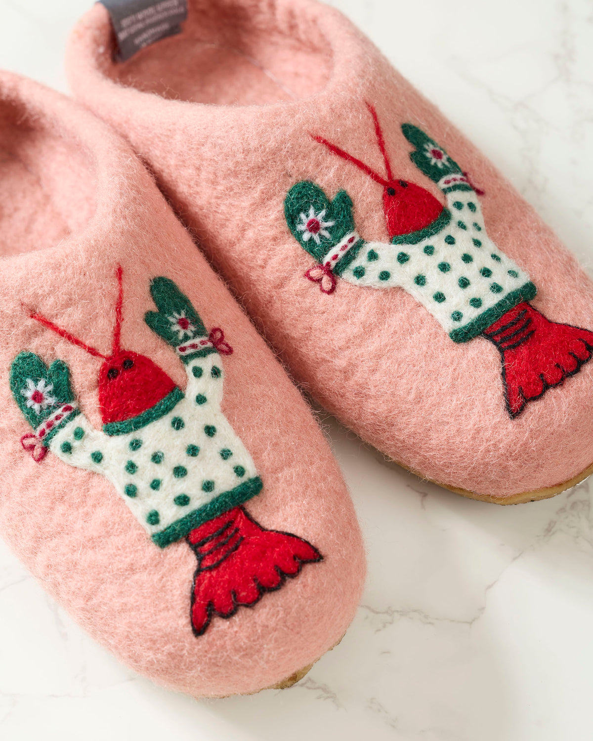 Close-up of pink slippers showing embroidered lobster characters with green mittens, white dotted sweaters, and red tails.