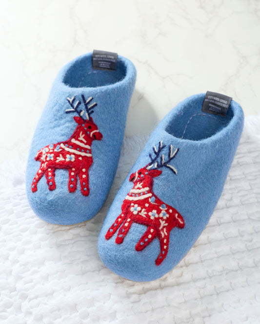 Pair of light blue slippers with red reindeer decorations shown on a white textured surface.