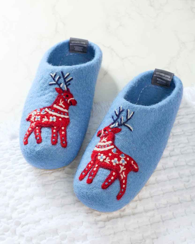 Pair of light blue slippers with red reindeer decorations shown on a white textured surface.