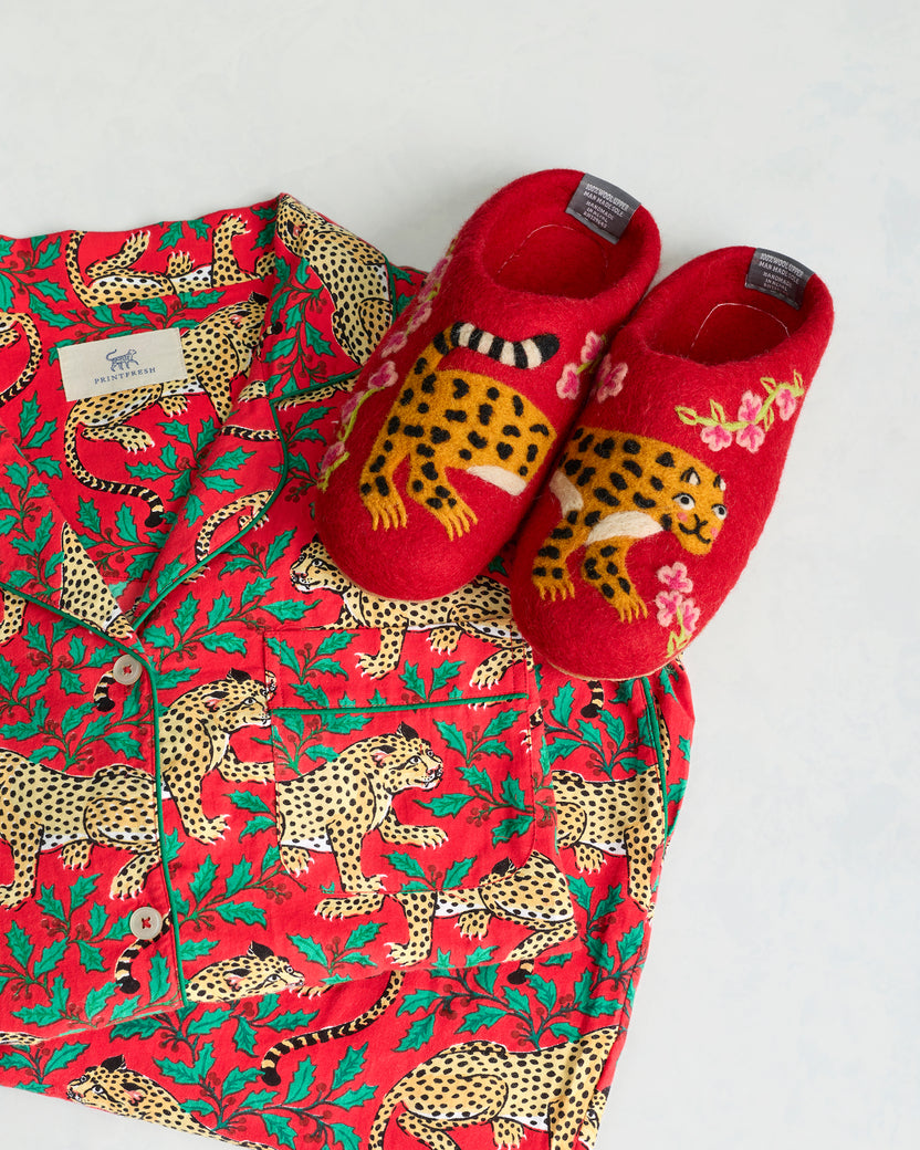 Close-up of red Winter Holly Bagheera slippers with felted leopard motifs beside the red leopard-print pajama set.