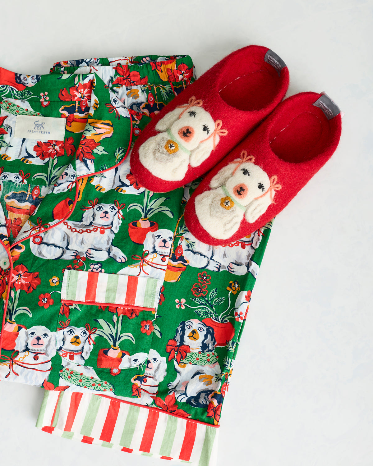 Close-up of red Good Dog Christmas slippers with felted dog motifs beside the green pajama set.