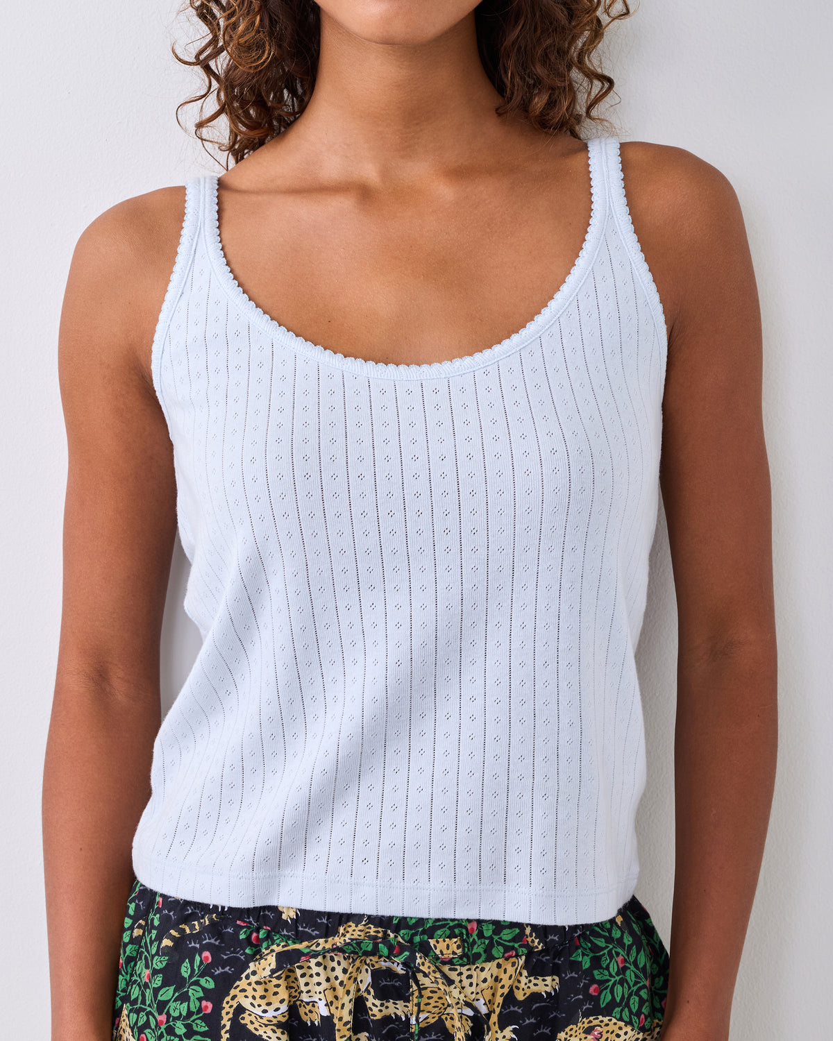 Light blue sleeveless pointelle tank top with lace-trimmed neckline and shoulder straps, shown on a person.