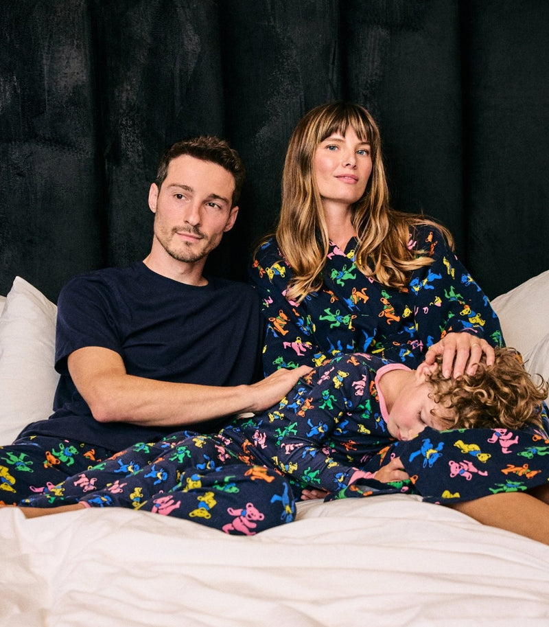 Three people relaxing together on a bed, with two wearing matching dark patterned pajamas.