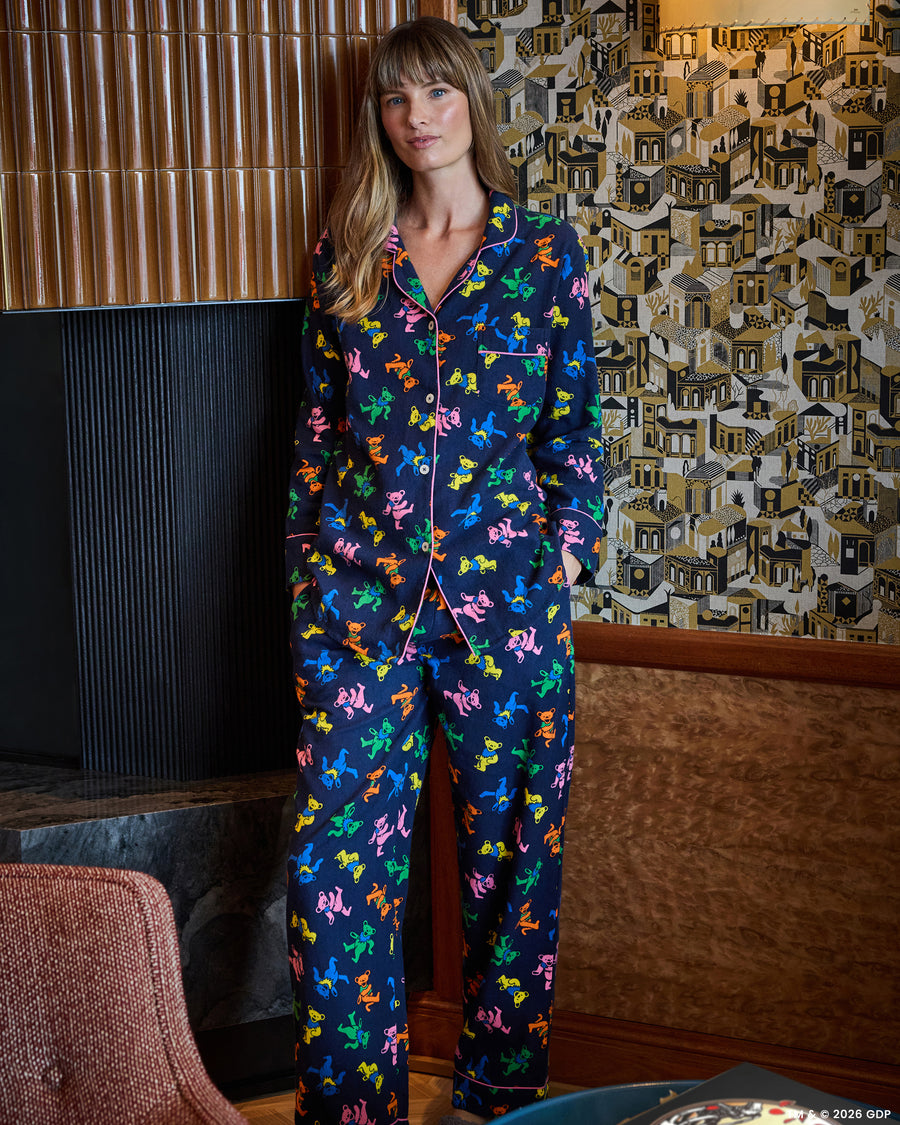 Full-body view of a person wearing a navy long pajama set with a multicolor dancing-bear print, button-front top, and long pants.