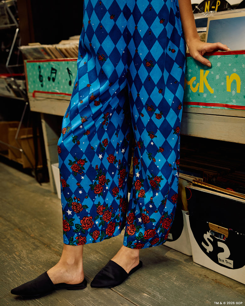 Close view of the blue argyle-print jumpsuit legs with rose and star motifs, paired with black flats.