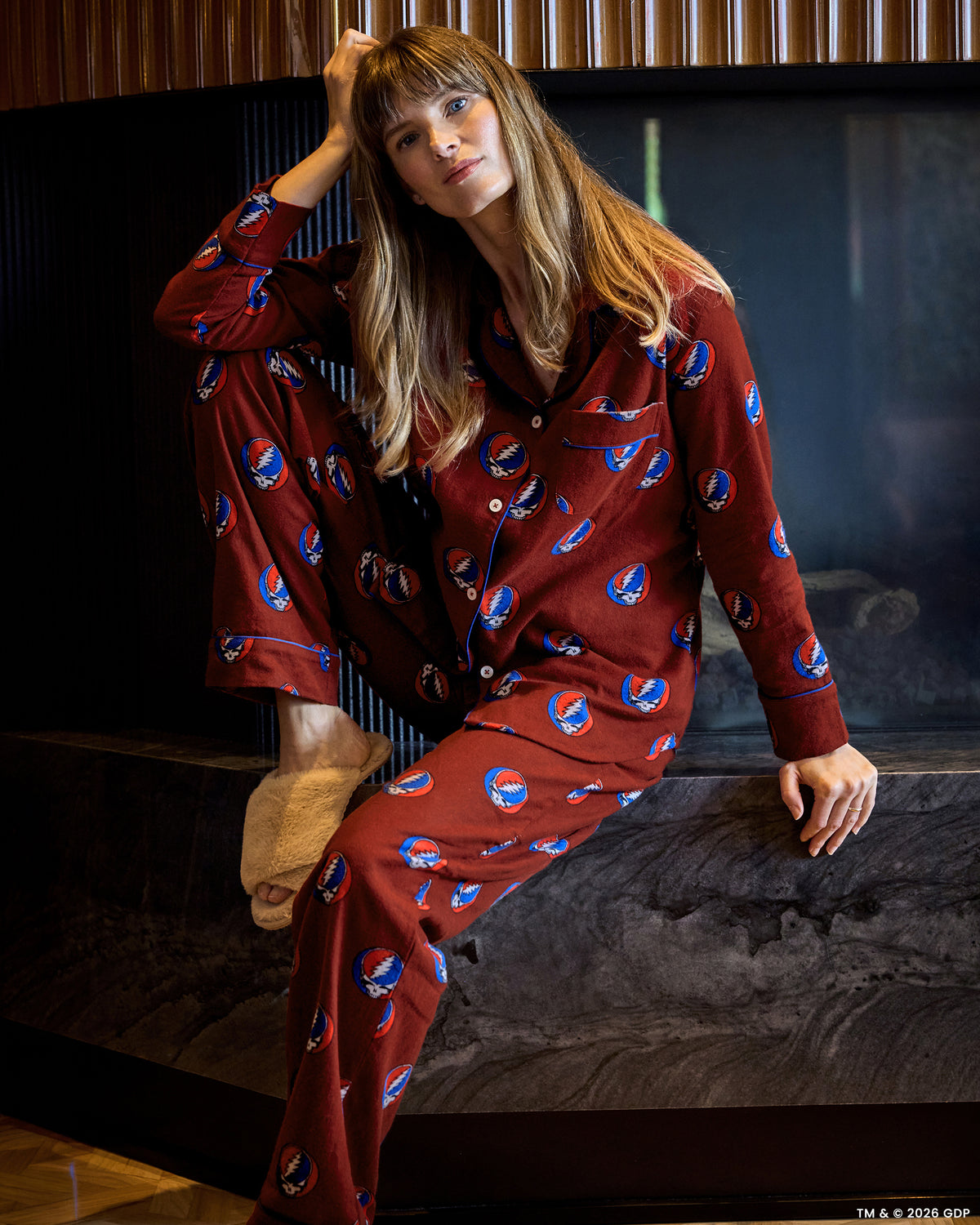 Person seated wearing a red long-sleeve pajama set with a repeated skull-and-lightning-bolt print.