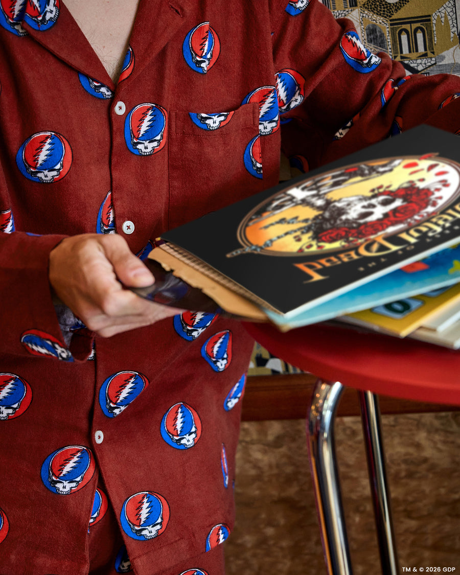 Close-up of a red long-sleeve pajama top with a skull-and-lightning-bolt print while a person holds books beside a table.