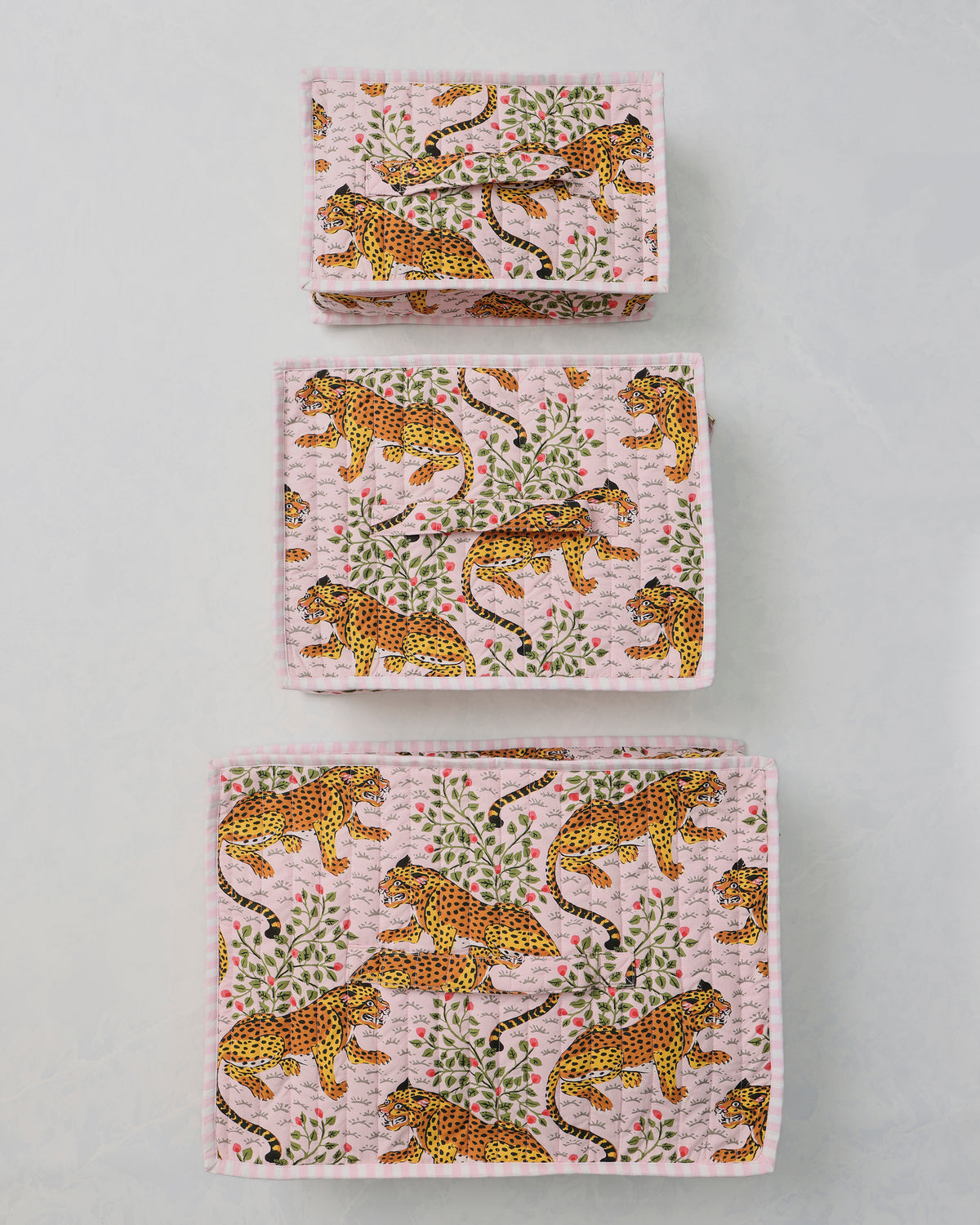 Three pink packing cubes with a leopard-and-leaf print arranged separately on a light background.