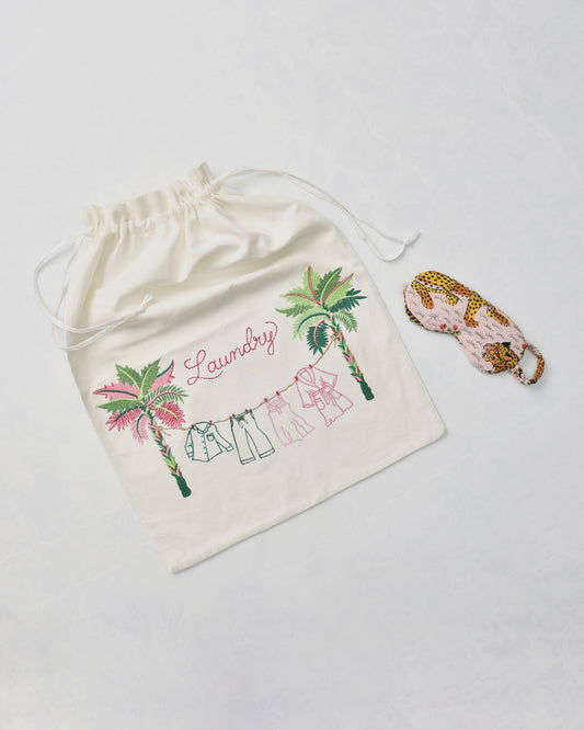 Embroidered drawstring laundry bag with palm trees, clothing line, and the word “Laundry,” beside a leopard-print eye mask.