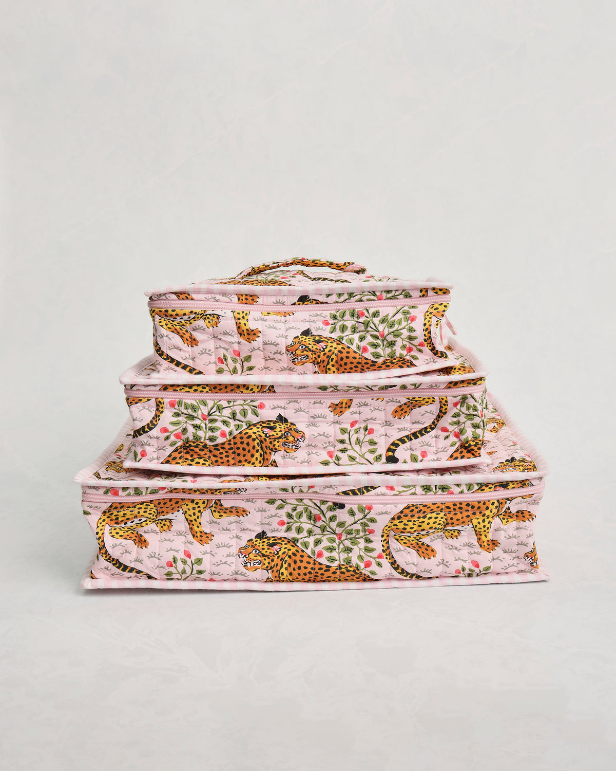 Three pink leopard-and-leaf print packing cubes stacked by size.
