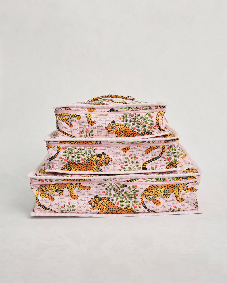 Three pink leopard-and-leaf print packing cubes stacked by size.