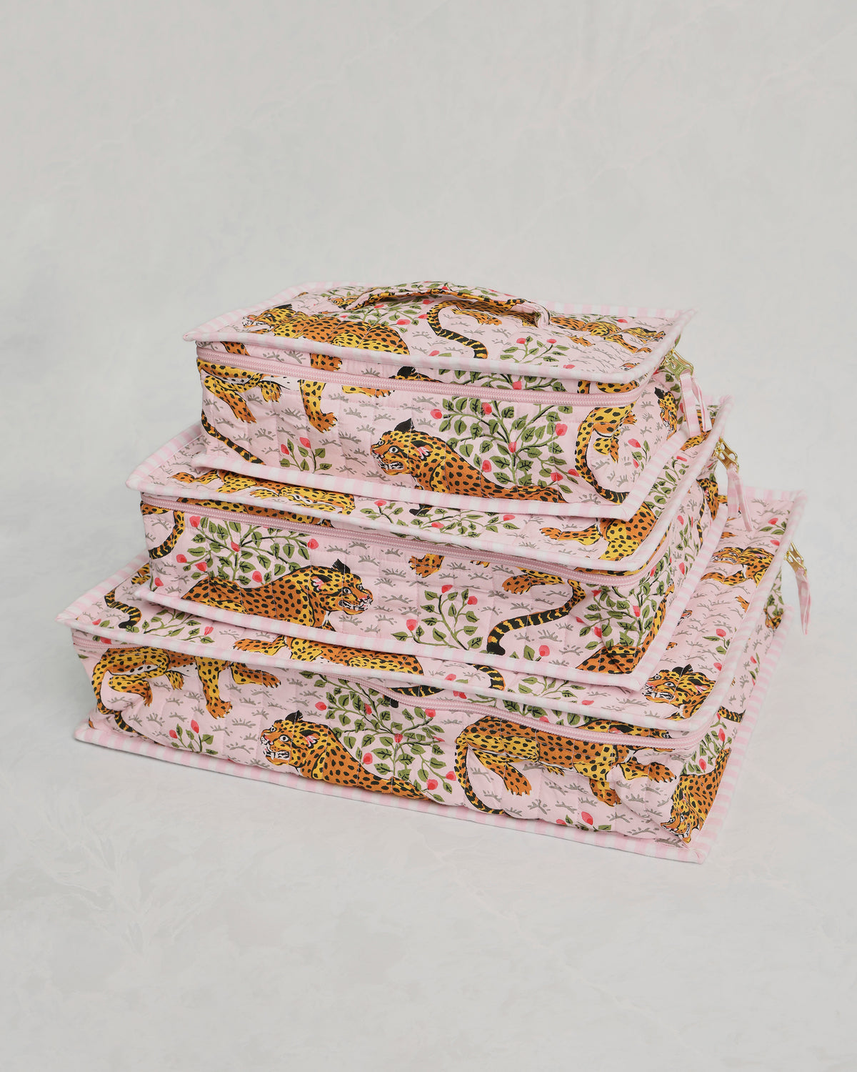 Three pink leopard-and-leaf print packing cubes stacked at an angle, showing their sides and zippers.