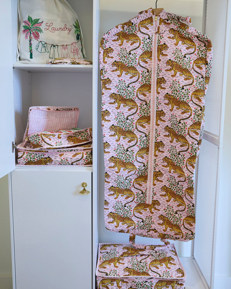 Bagheera blush garment bag hanging in a closet beside matching printed storage items.