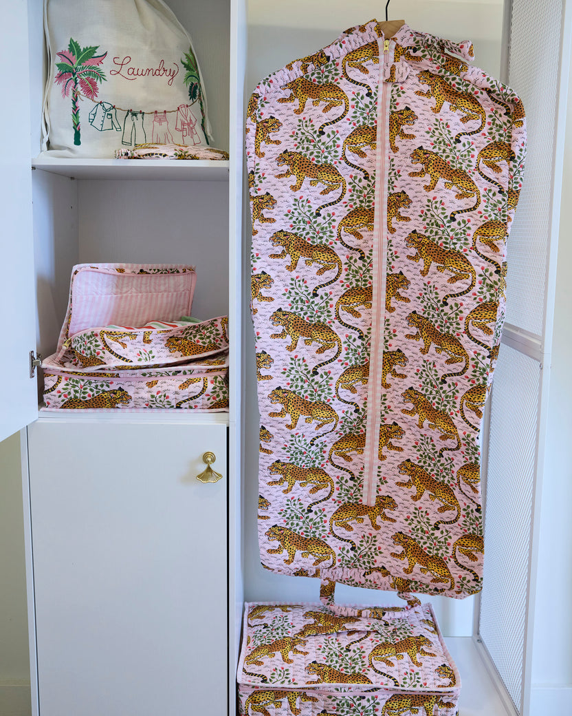 Bagheera blush garment bag hanging in a closet beside matching printed storage items.