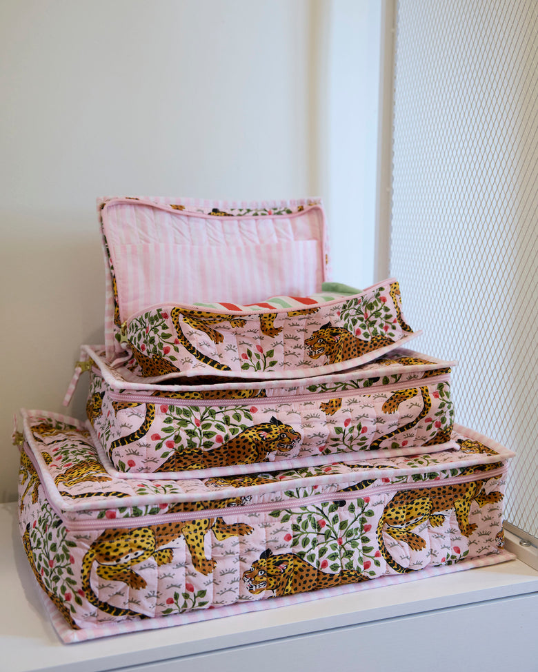 Three pink leopard-and-leaf print packing cubes stacked with the top cube open.