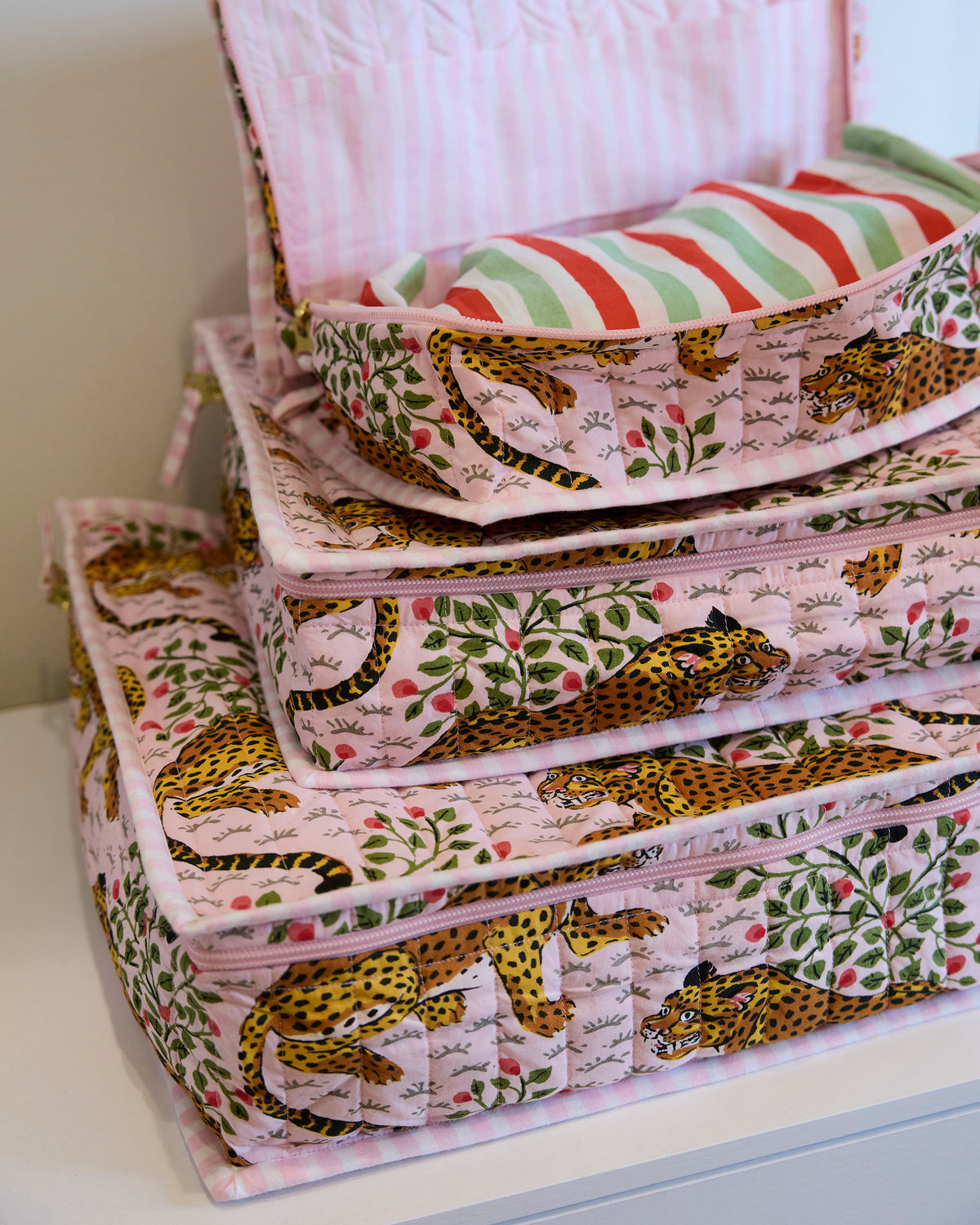 Close view of stacked pink leopard-and-leaf print packing cubes, with the open top cube holding a striped garment.