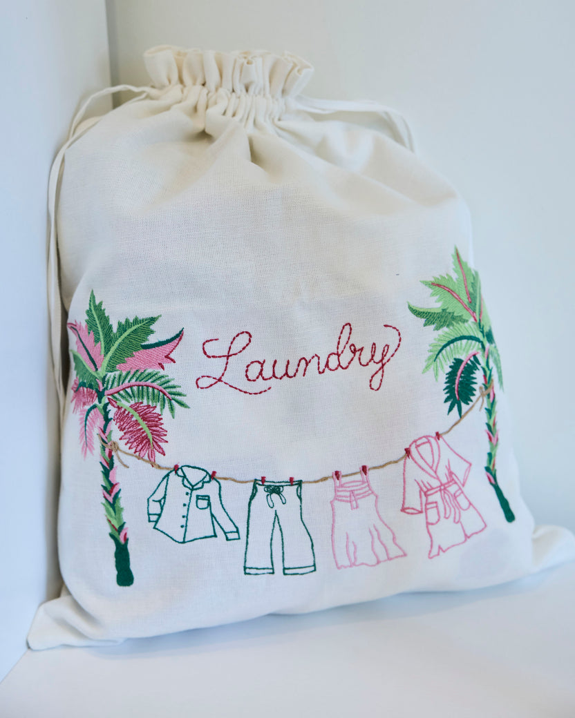 Drawstring laundry bag embroidered with the word “Laundry,” palm leaves, and clothes hanging on a line.