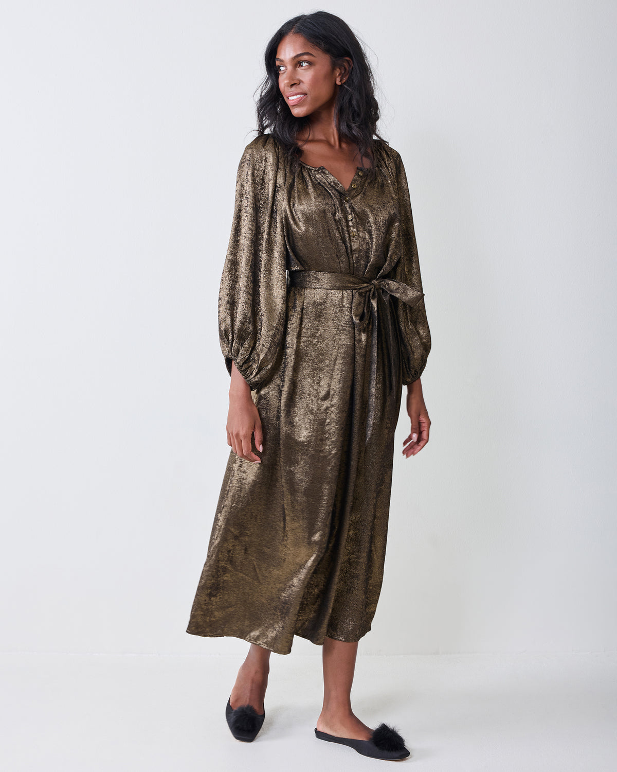 Person wearing a gold long-sleeved dress with a buttoned neckline, waist tie, and flowing skirt.