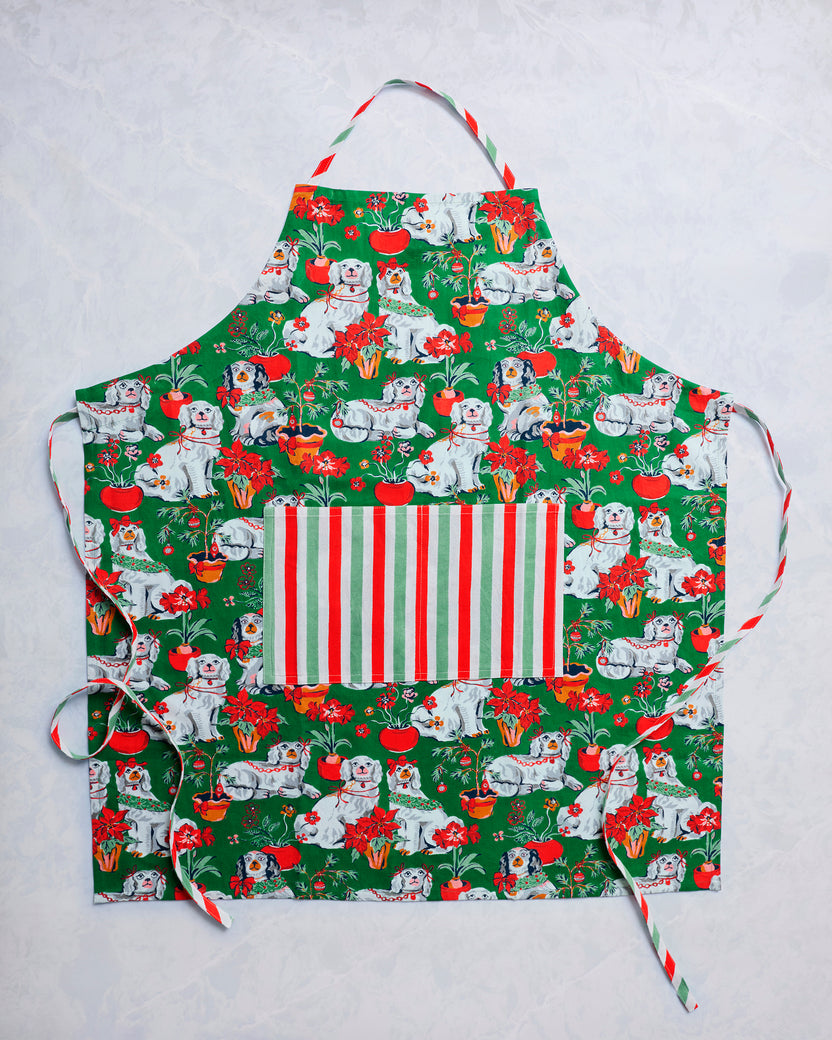Green Good Dog Christmas apron with an all-over dog and holiday plant print, striped front pocket, and neck strap