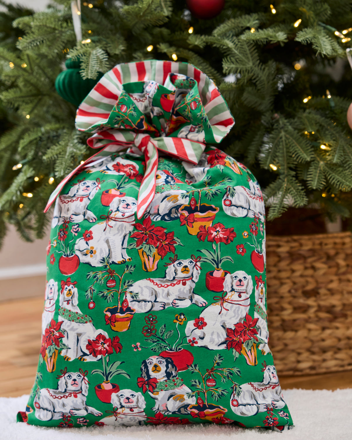 Green Christmas gift sack with a coordinating red, white, and green striped tie, displayed in front of a decorated tree.