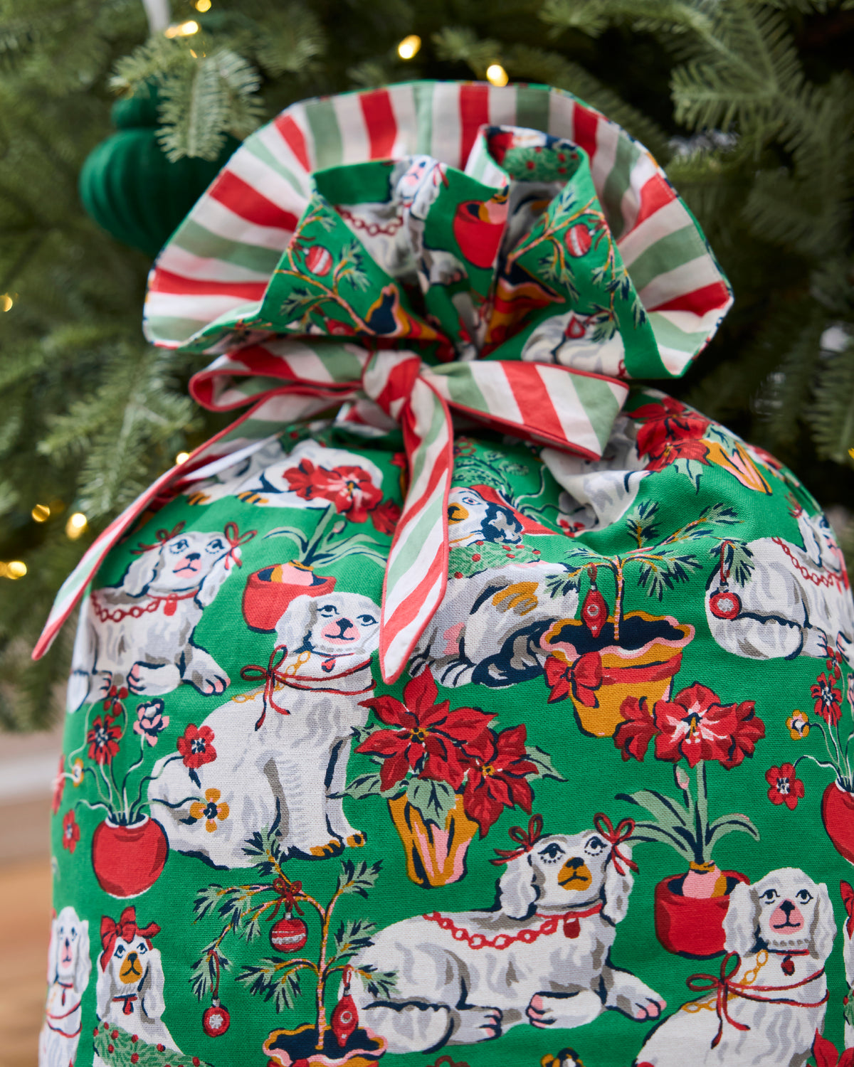 Close-up of the green Christmas gift sack showing its striped tie and dog, poinsettia, and holiday plant print.