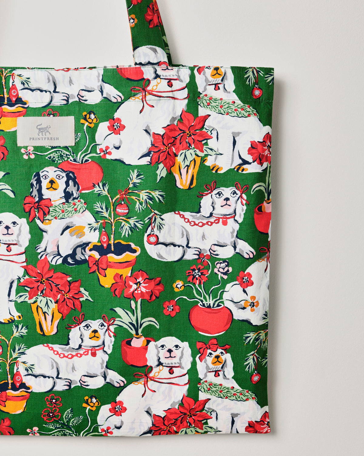 Close view of the Good Dog Christmas tote’s evergreen print, showing white dogs, red flowers, potted plants, and the Printfresh label.