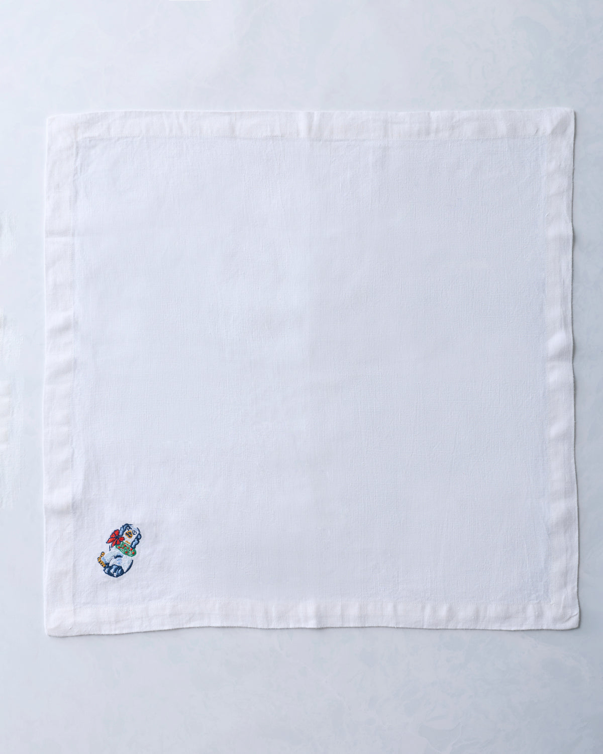 Single white dinner napkin with a small embroidered dog figurine near one corner