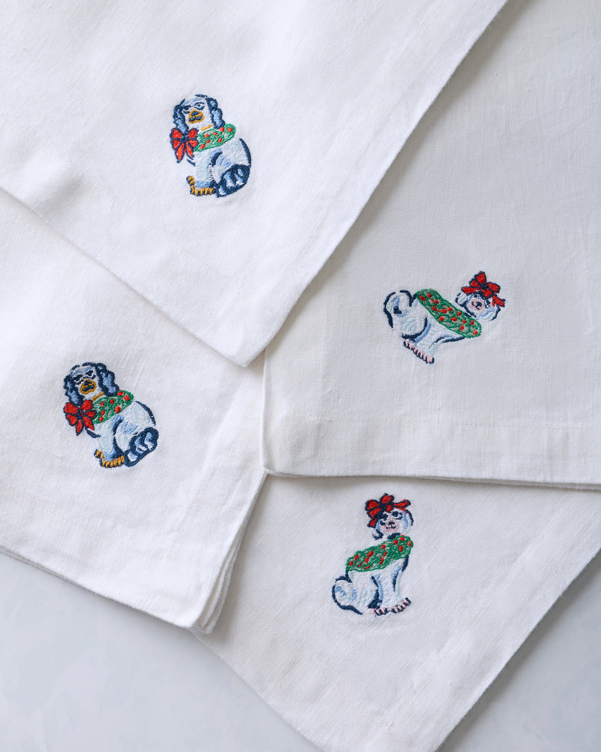 Four white dinner napkins with embroidered dog figurine designs