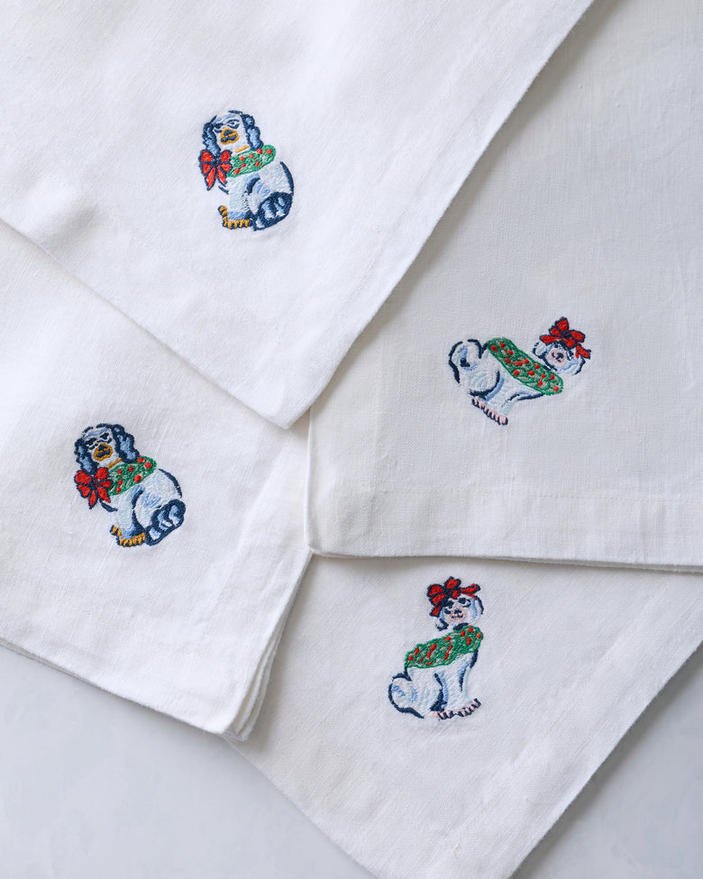 Four white dinner napkins with embroidered dog figurine designs