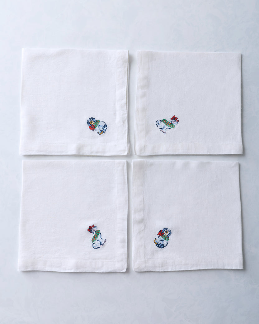 Set of four white dinner napkins arranged in a square, each with an embroidered dog figurine