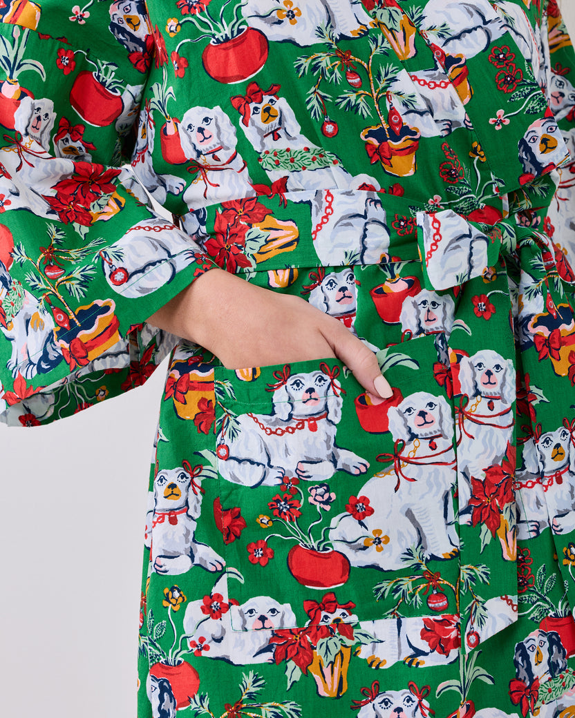 Close-up of a green long robe with a festive print of white dogs, poinsettias, ornaments, and red pots; a hand rests in the pocket.