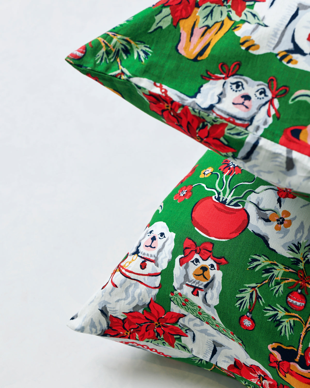 Close-up of an evergreen pillowcase showing the printed white dogs, red poinsettias, potted plants, and holiday details.