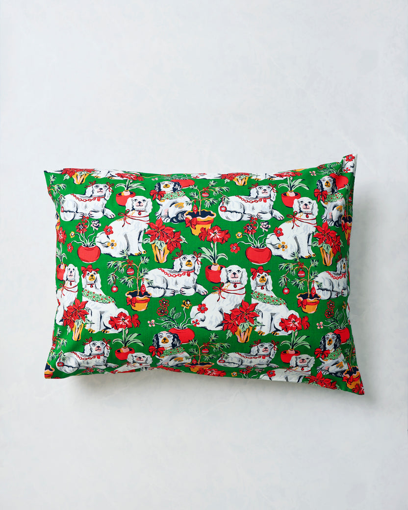 Evergreen pillowcase displayed flat with a repeating print of white dogs, red poinsettias, potted plants, and holiday decorations.