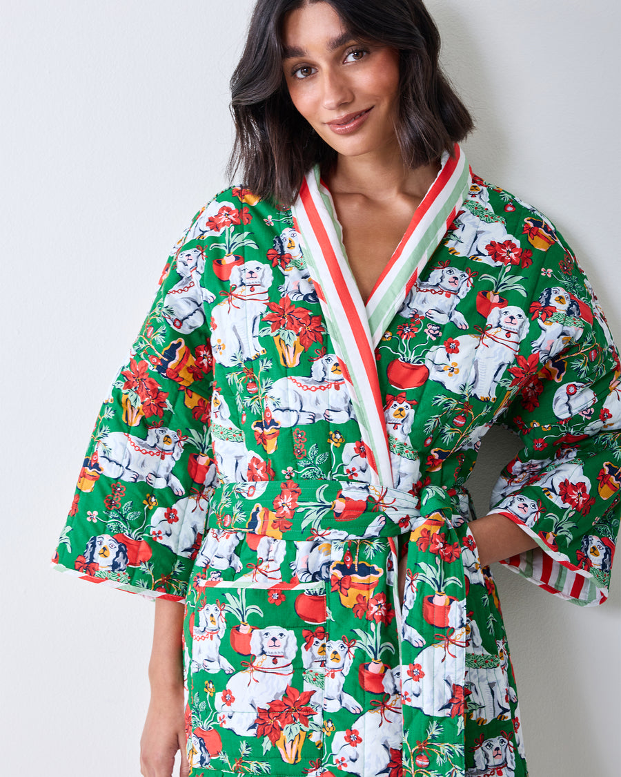 Front view of a person wearing a green reversible quilted robe patterned with Christmas dogs, flowers, and holiday motifs.