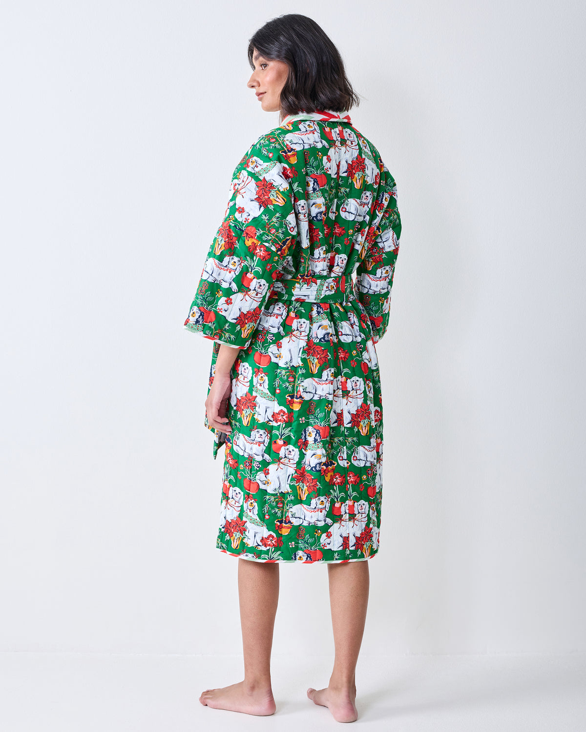 Back view of a person wearing a green robe covered in Christmas dog and holiday motifs.