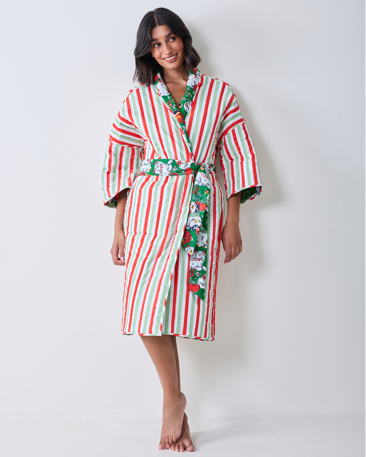 Front view of a person wearing the striped side of a reversible quilted robe with a green patterned belt and trim.