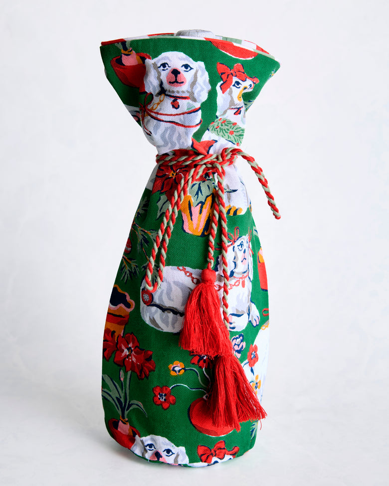 Green Christmas wine bag with dog illustrations, a braided tie, and red tassels, shown standing upright.